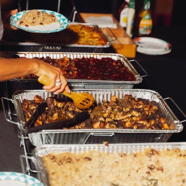 A person serving themselves Jamaican rice and peas, jerk chicken, and other dishes from a buffet.
