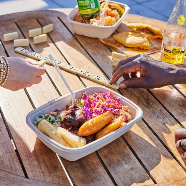 Two people playing dominoes on a wooden table with Jrk! Jamaican food and drinks.