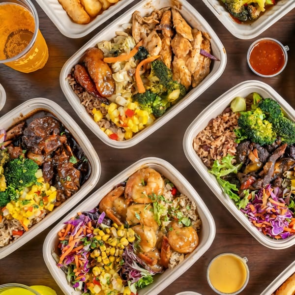 Overhead view of multiple Jrk! Jamaican bowls with various meats, rice, and vegetables.