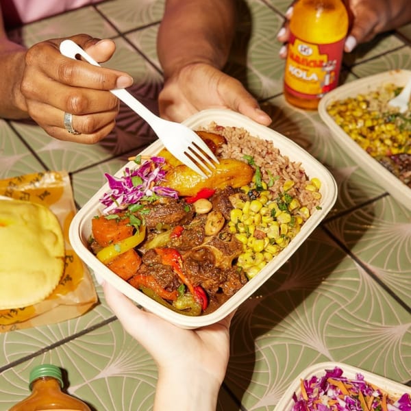 Hands sharing a Jamaican oxtail and rice bowl with plantains, corn, and cabbage slaw.